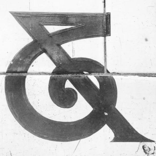 Sculptural serif letterform with high contrast, monochrome, brutalist, dark