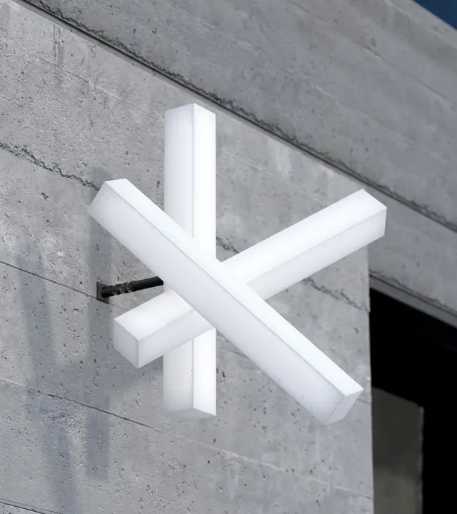 Kobase asterisk mark as a white projecting sign on concrete, minimal, architectural, light