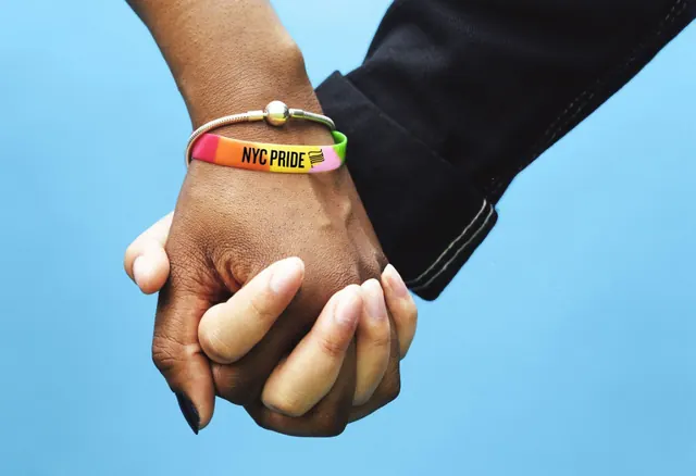 NYC Pride wristband on clasped hands, photographic, minimal, vibrant