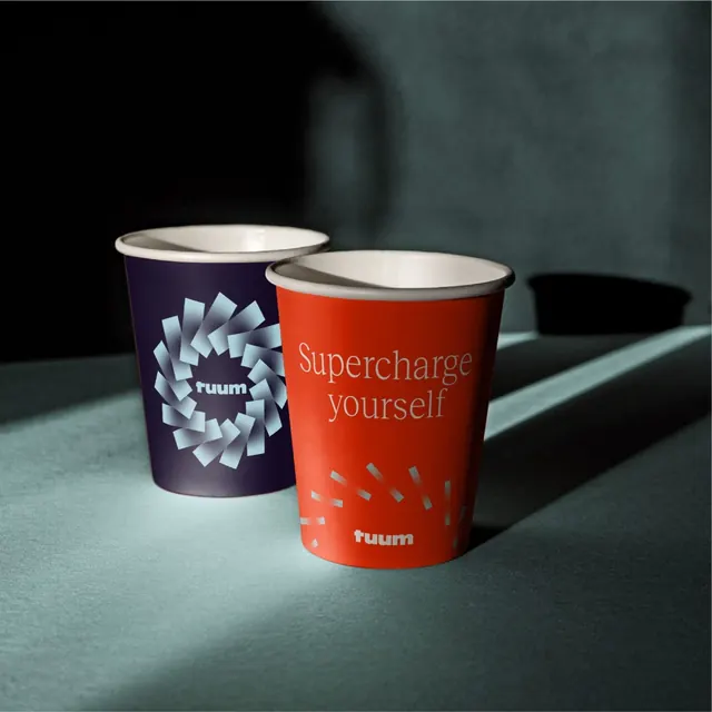 Tuum branded paper cups in raking light, photographic, cinematic, dark