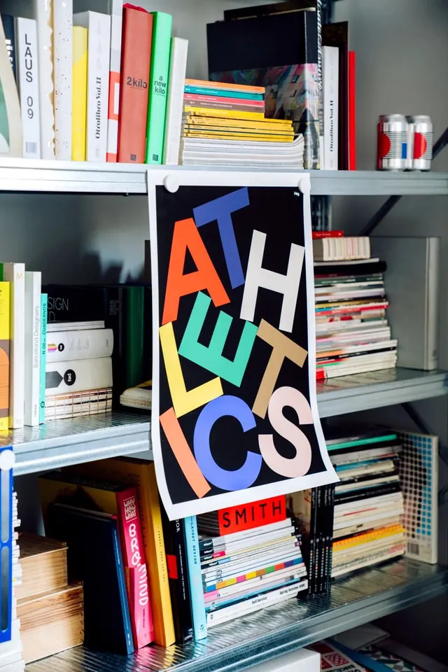 Colorful typography poster leaning against design books on shelving, geometric, flat, vibrant