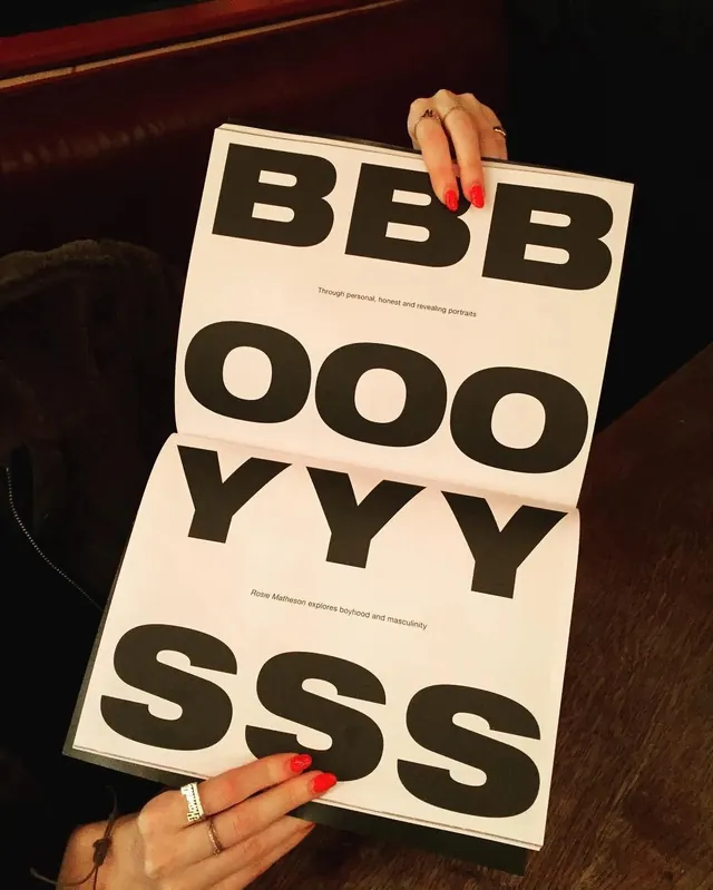 Stacked typographic publication cover BBBOOOYYY held in hand, photographic, minimal, dark