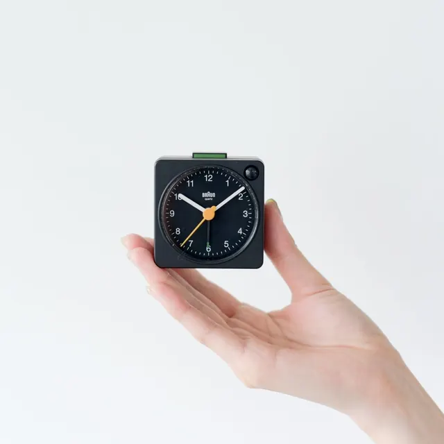 Braun minimalist square clock in hand, high contrast studio shot, minimal, technical, dark