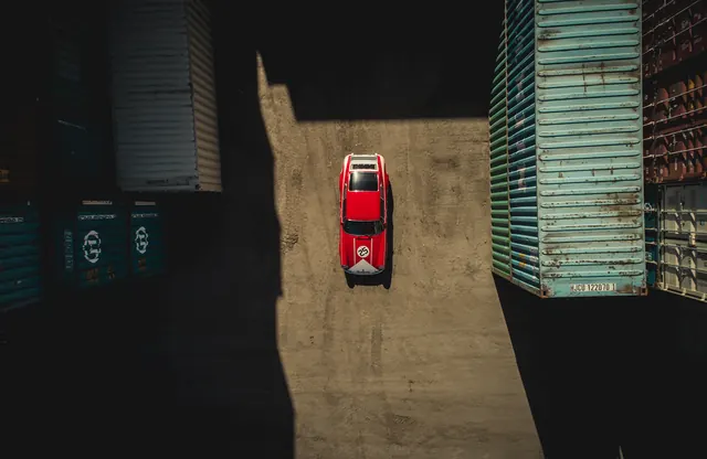 Red Car in Shipping Container Yard, minimal, dark-mode, dark