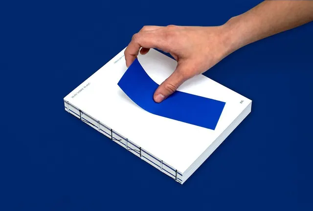 Hand Placing Blue Ribbon on White Book Mockup, minimal, corporate-clean, high-contrast