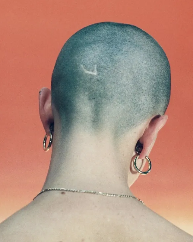 Close-up of a person with a shaved head and piercings, minimal, photographic, vibrant