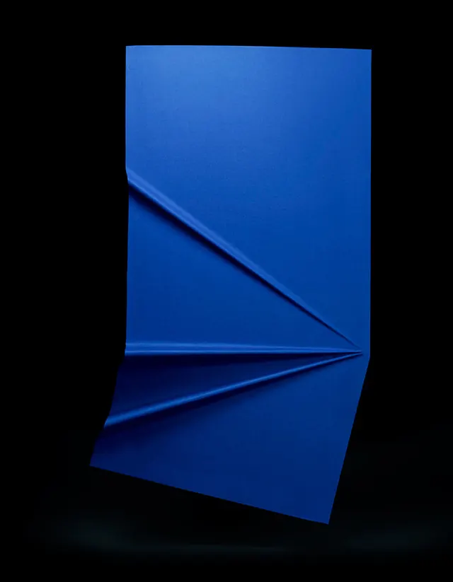 Folded blue paper sculpture against black, minimal, geometric, vibrant
