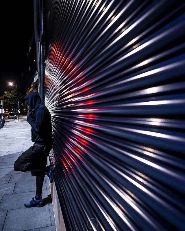 Person standing by corrugated metal wall, dark-mode, photographic, dark