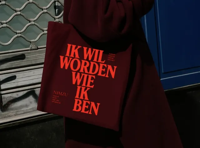 Typographic tote bag with Dutch phrase and bold red display type, minimal, dark