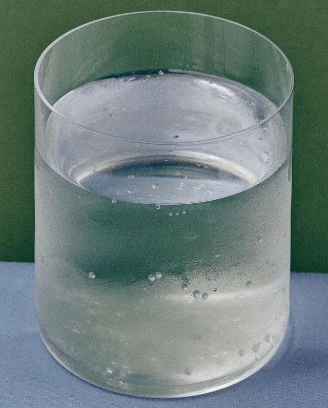 Clear glass of water with ice and bubbles on green and white background, photographic, minimal, light