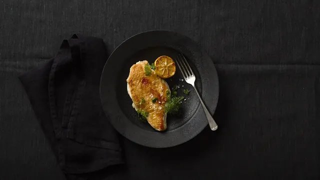Food plating on black plate with lemon garnish, photographic, minimalist, dark
