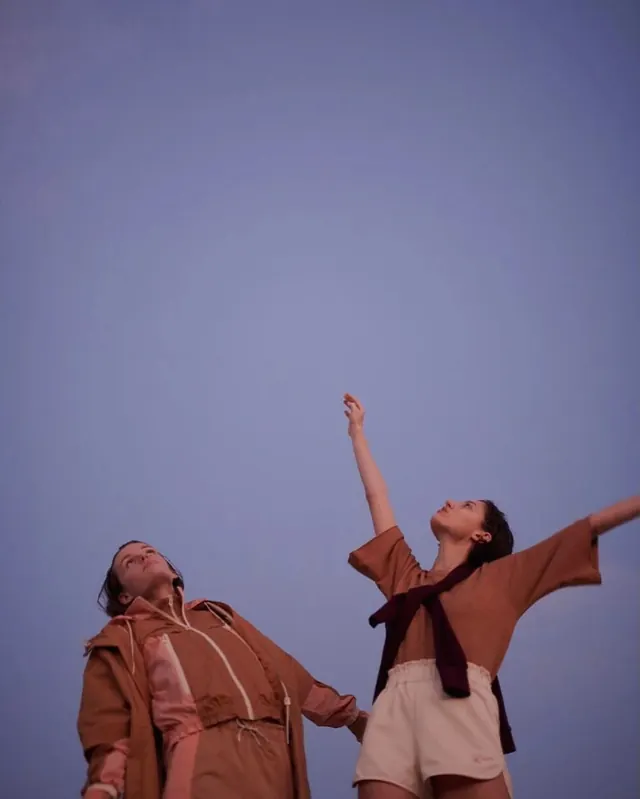 Two figures against blue sky with raised arms, photographic, editorial, warm