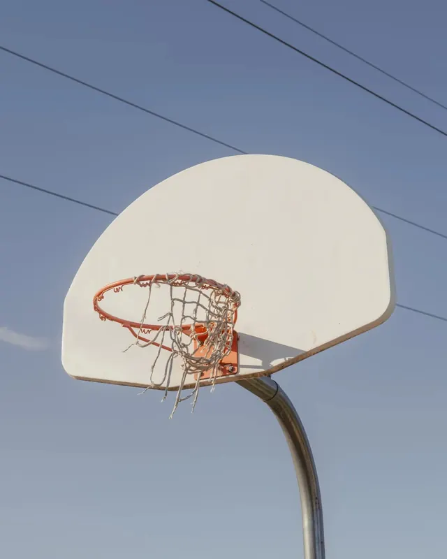 Weathered basketball hoop against blue sky, minimal, photographic, cool