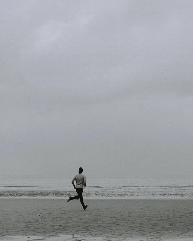 Solitary figure running on empty beach, photographic, minimal, muted