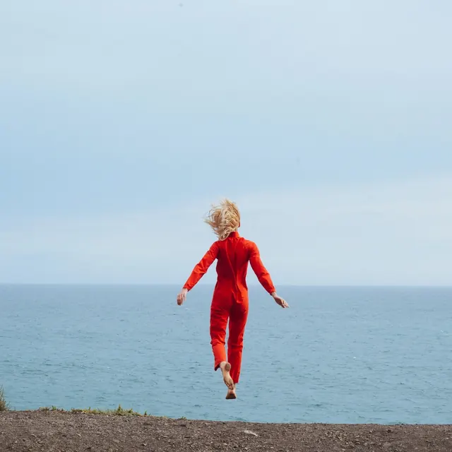 Orange jumpsuit cliff jump portrait, photographic, editorial, vibrant