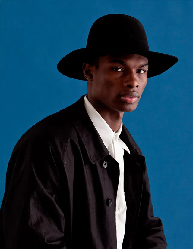 Fedora portrait on cobalt backdrop, editorial, photographic, vibrant