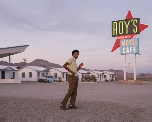 Man in vintage clothing posed at retro Route 66 motel signage, photographic, retro, warm