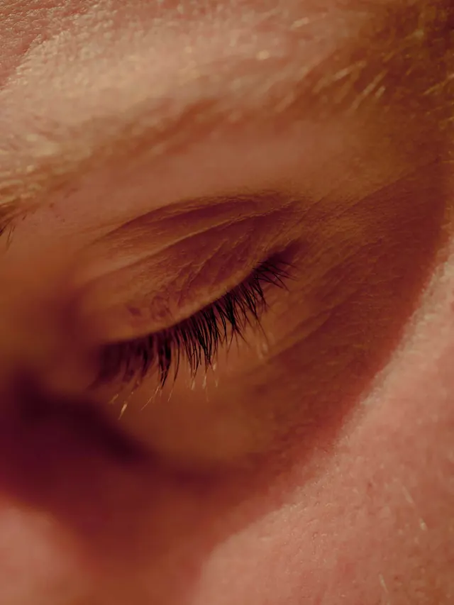 Extreme close-up of closed eyelid with lashes and texture, photographic, editorial, warm