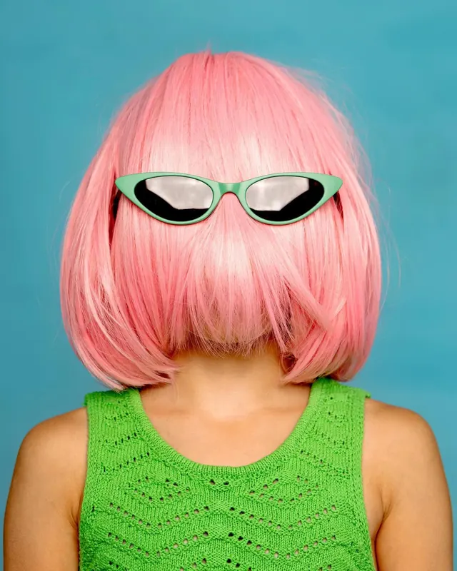 Figure with pink wig and cat-eye glasses on turquoise background, photographic, pop-art, vibrant