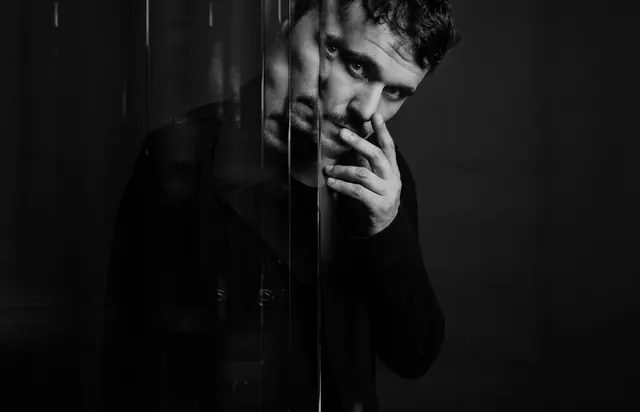 Moody black and white male portrait with metal grid, photographic, editorial, monochromatic