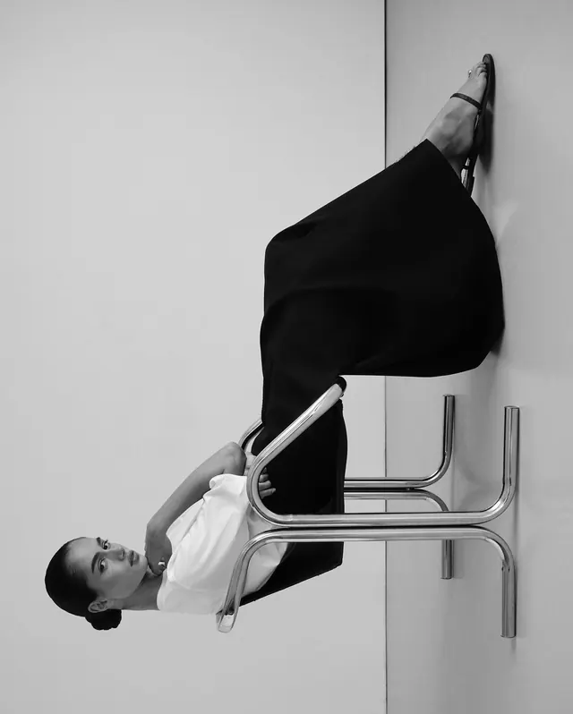 Black and white portrait of person on minimalist furniture, photographic, editorial, monochromatic