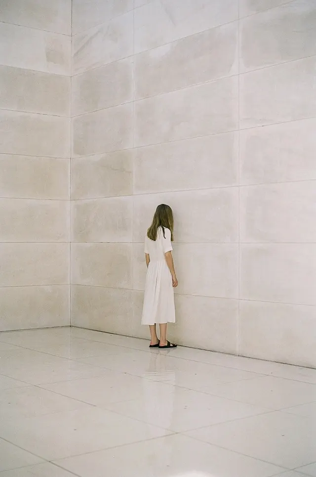 Woman in white dress against textured wall, minimal, photographic, light