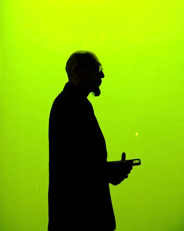 Figure silhouette holding device against neon lime, photographic, minimal, vibrant