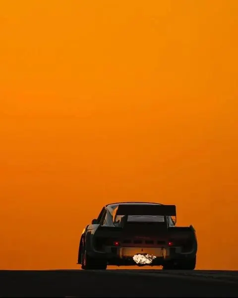 Black sports car against bright orange sky, photographic, minimalist, dark