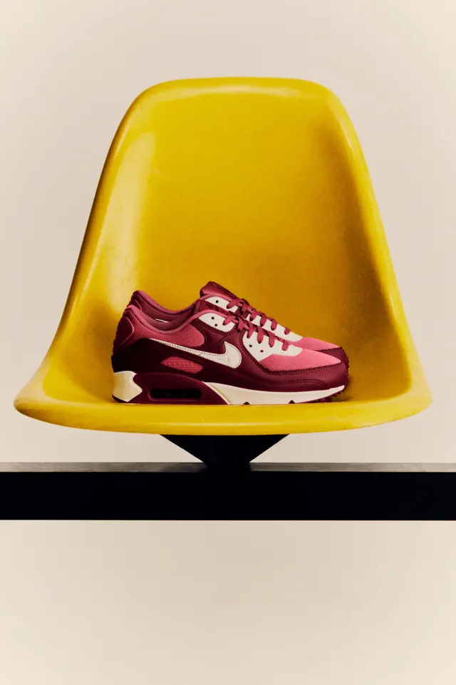 Burgundy sneaker nestled in yellow chair against cream background, photographic, minimalist, warm