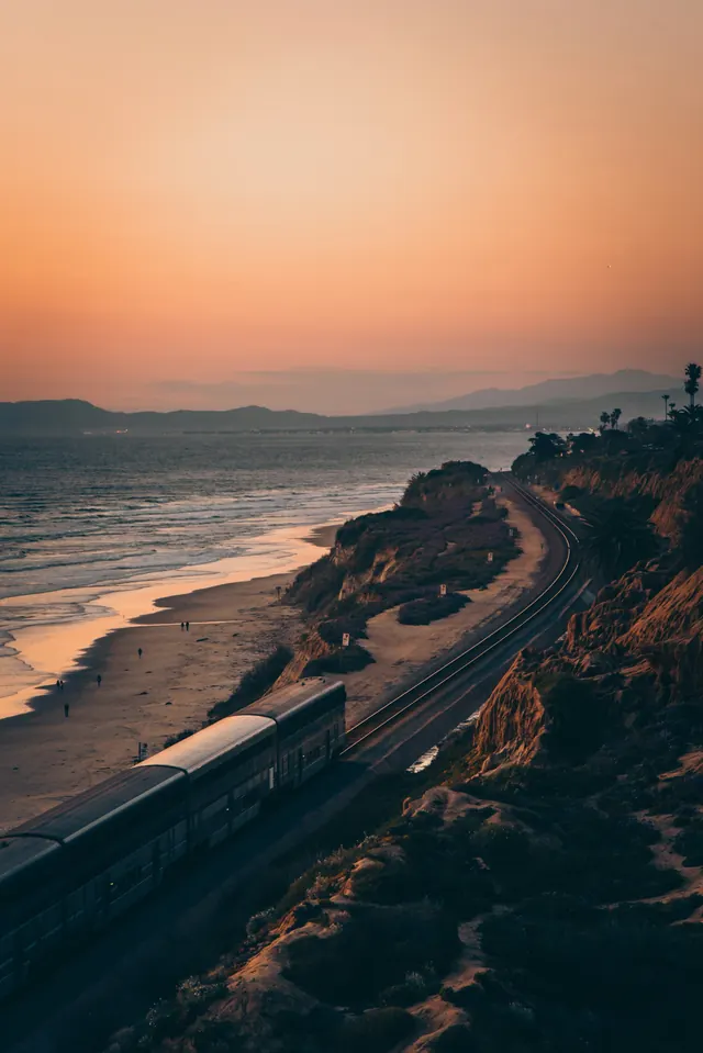 Train passing coastal cliff at sunset, photographic, organic, warm