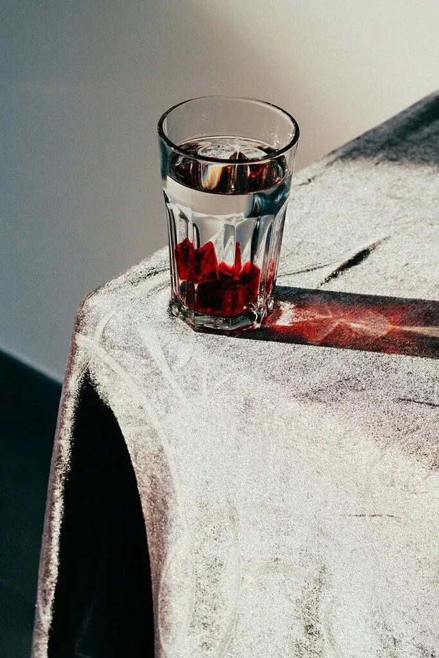 Glass of red liquid with shadow on textured surface, photographic, minimalist, light