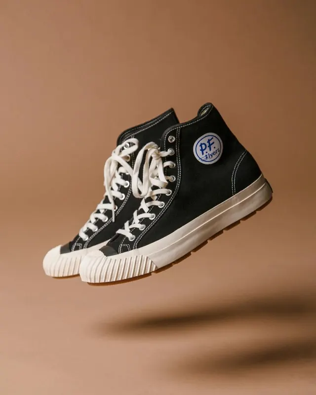 Black high-top sneaker with cream sole on tan background, photographic, minimalist, warm