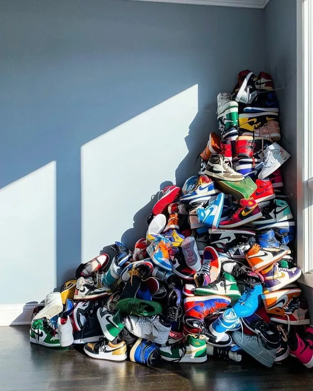Stacked sneaker collection against blue wall, photographic, minimalist, vibrant