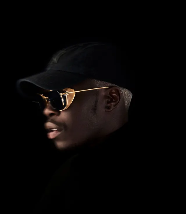 High-contrast portrait with gold-rimmed sunglasses, photographic, minimal, dark