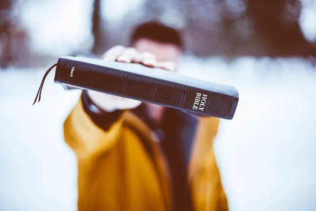 Hands holding Holy Bible in snowy landscape, photographic, minimal, cool