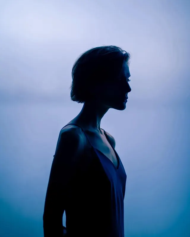 Silhouette profile of woman against hazy blue sky, photographic, minimal, dark