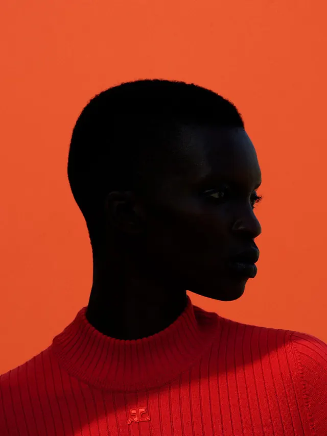 Profile portrait of model in red turtleneck against orange, photographic, editorial, vibrant