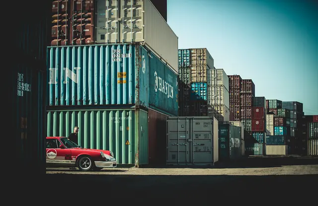 Red Porsche in front of stacked shipping containers, photographic, editorial, vibrant