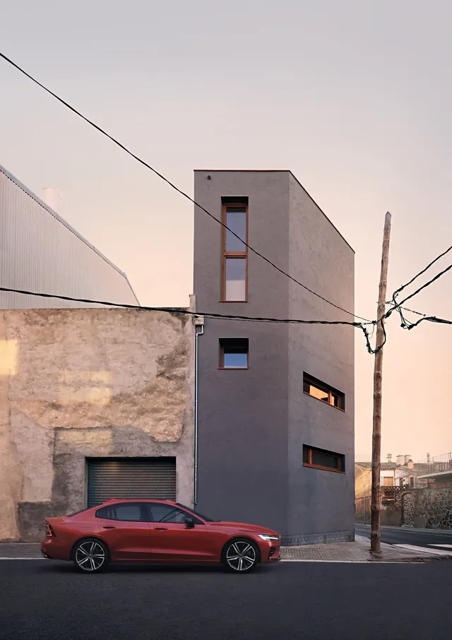 Red Volvo sedan parked before modern concrete building, photographic, minimal, muted
