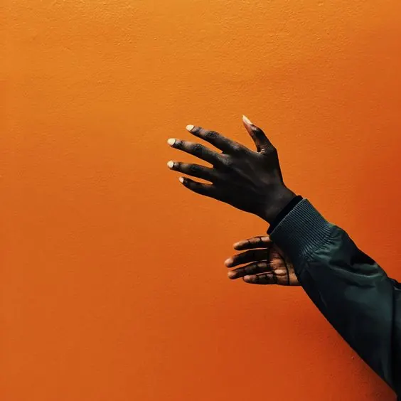 Elegant hand against vibrant orange wall, minimal, photographic, vibrant