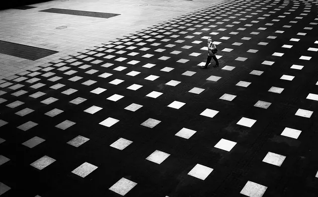 Solitary figure on vast geometric plaza, photographic, monochrome, monochrome