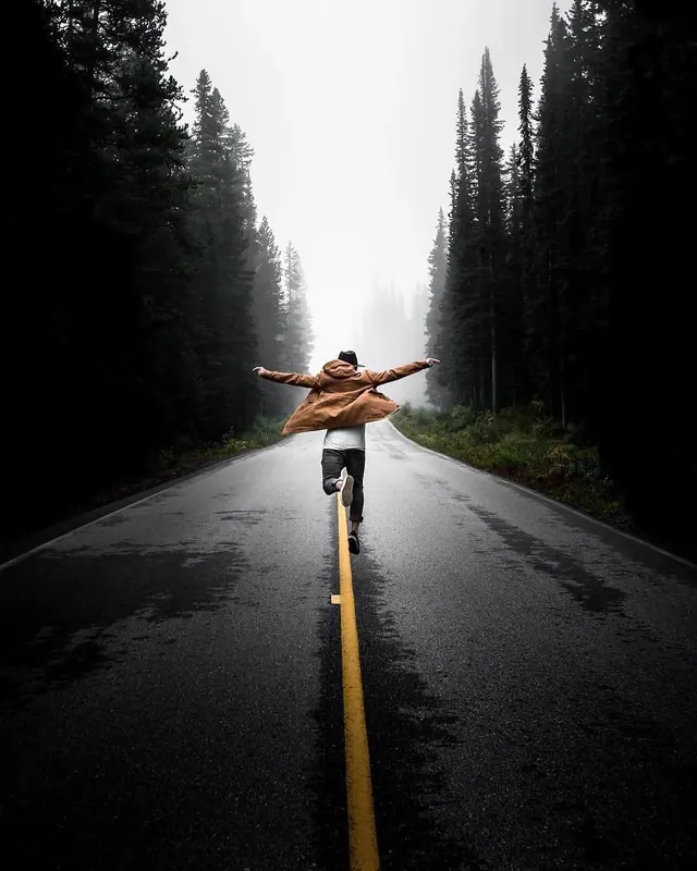 Person jumping on yellow line in misty forest road, photographic, editorial, dark