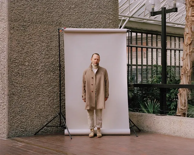 Fashion portrait of man in beige coat against paper backdrop, minimal, photographic, muted