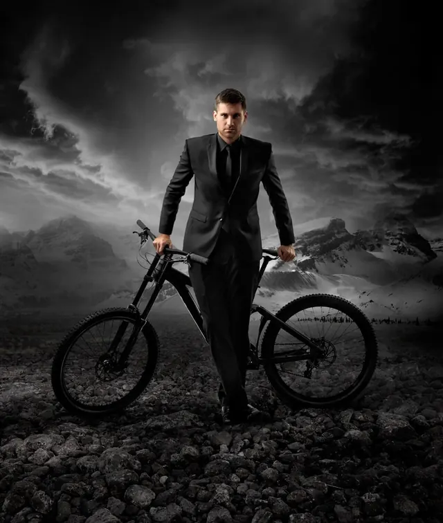 Man in suit with mountain bike in dramatic landscape, minimal, editorial, dark
