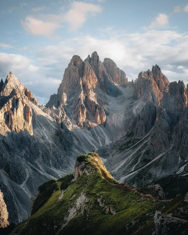 Dramatic alpine peaks with lone figure on grassy ridge, photographic, cool