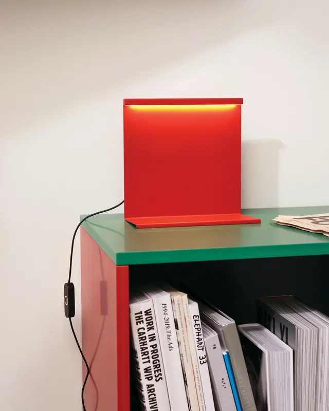 Red LBM table lamp glowing on green cabinet, minimal, vibrant