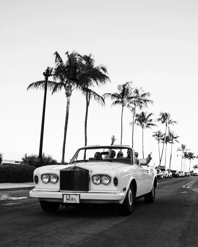 Vintage white Rolls Royce convertible on palm-lined road, minimal, photographic, monochrome