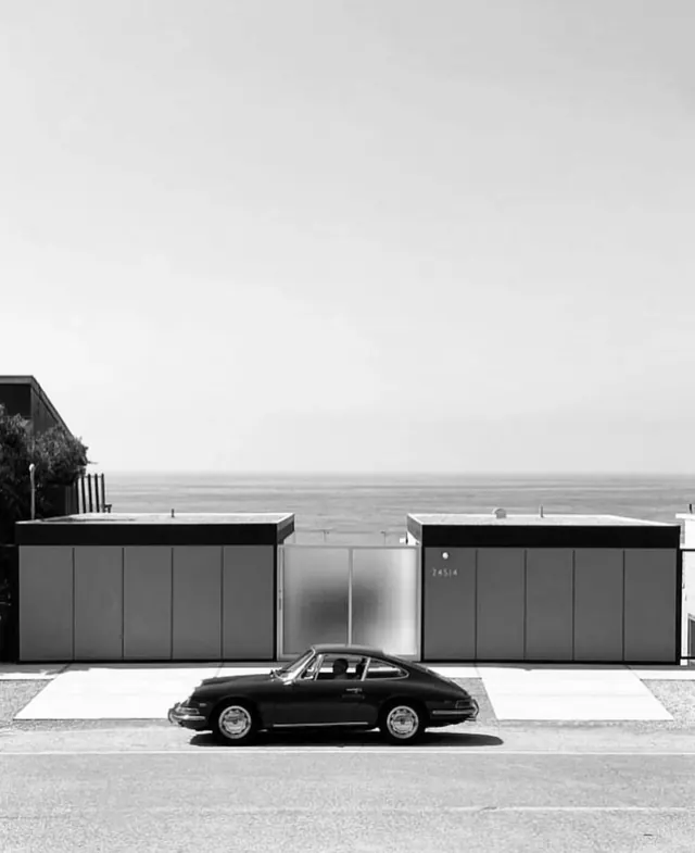 Vintage Porsche parked in front of minimalist garage structures, photographic, minimalist, monochrome