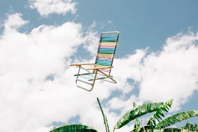 Colorful beach chair floating in blue sky above tropical plants, playful, photographic, vibrant