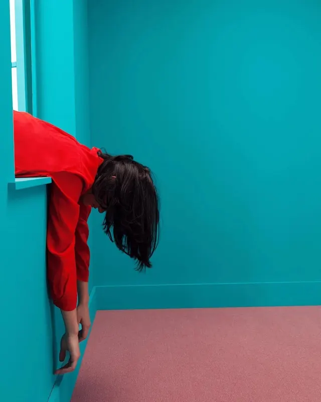 Person in red jacket leaning from teal window, photographic, bold, vibrant